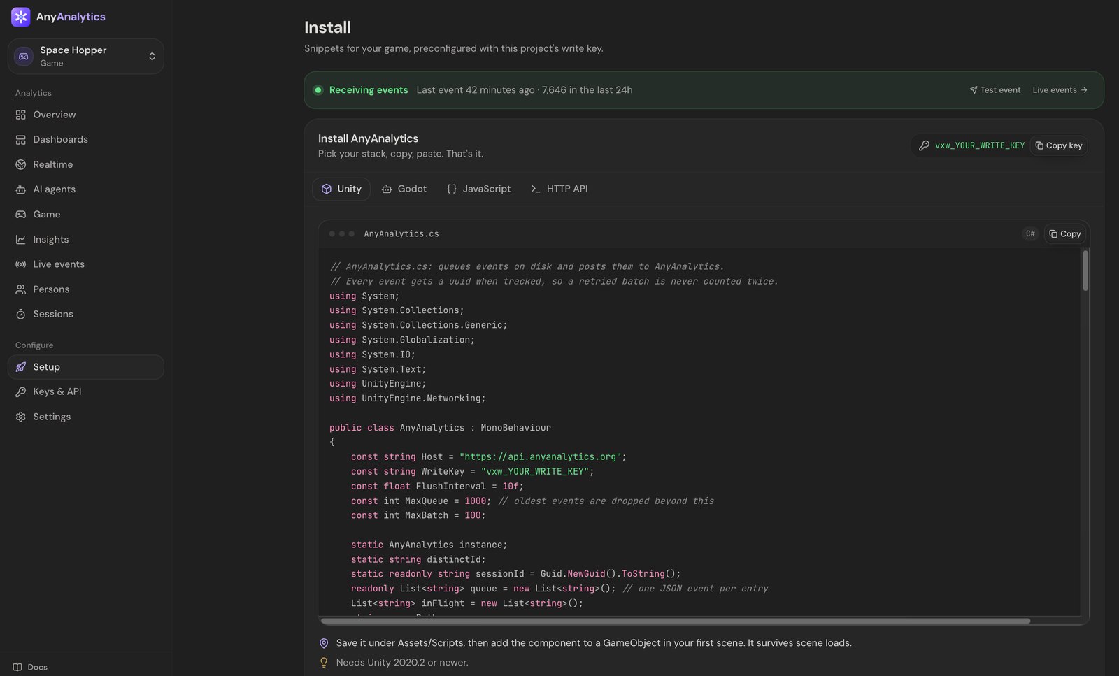 The AnyAnalytics Setup page with the Unity tab selected, showing the AnyAnalytics.cs script with the project's host and write key filled in, a Copy button, and the instruction to save it under Assets/Scripts and add the component to a GameObject in the first scene.
